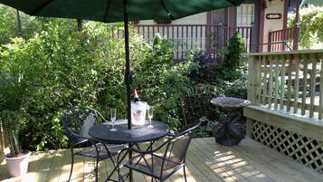 A wooden deck with a round metal table and chairs, a green umbrella, and a birdbath.