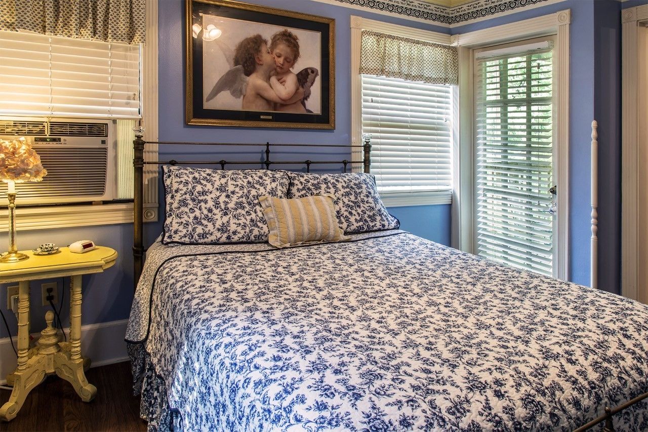 A bedroom with a floral bedspread, a bedside table with a lamp, and a framed picture on the wall.