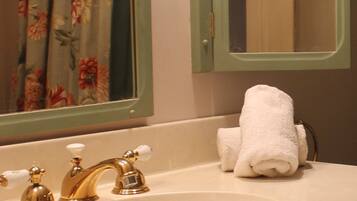 A bathroom with a sink, two gold faucets, a white towel, and a mirror reflecting a window with curtains.