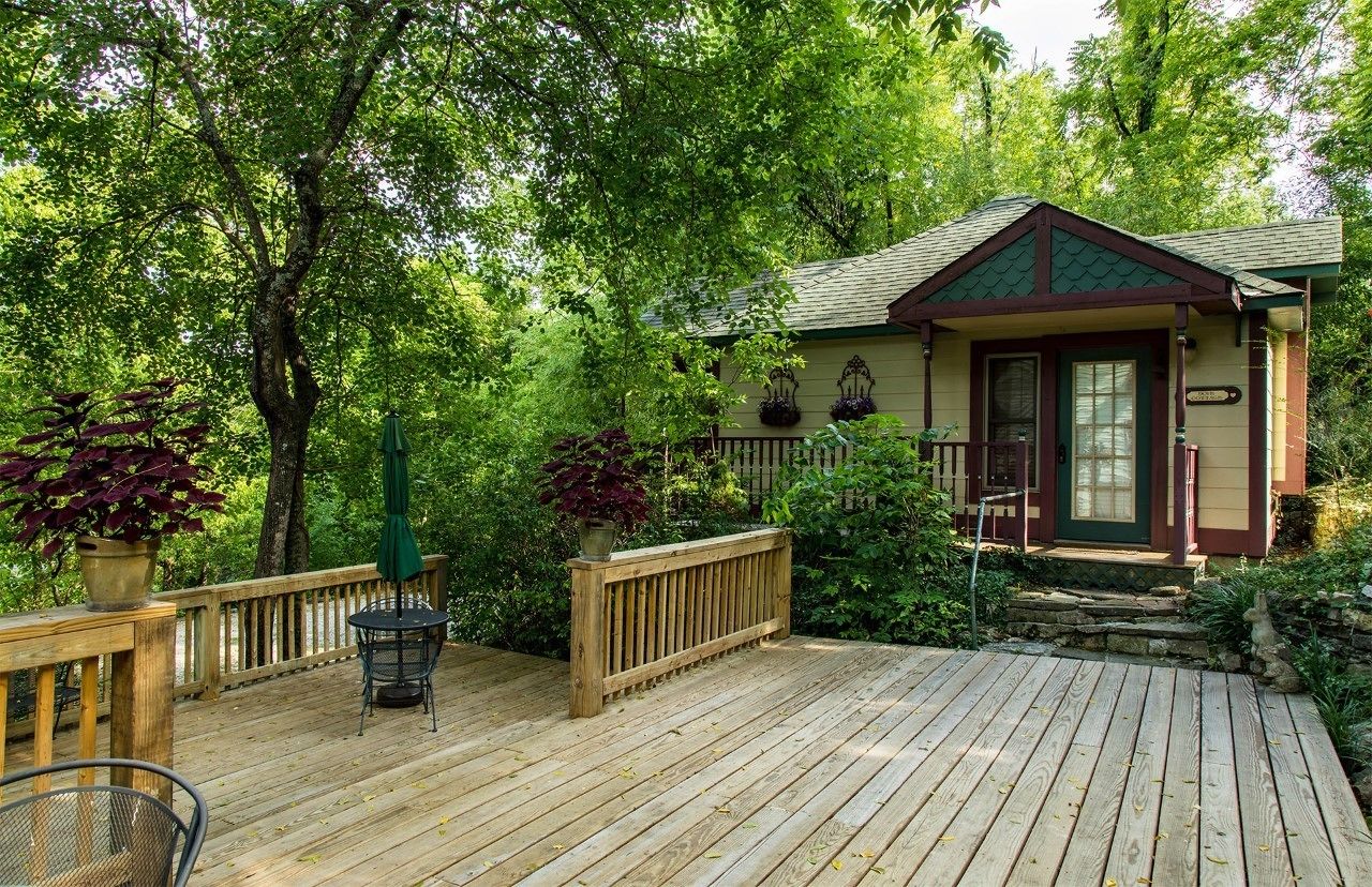 Une terrasse en bois avec un petit bâtiment, le tout entouré d’une végétation luxuriante.