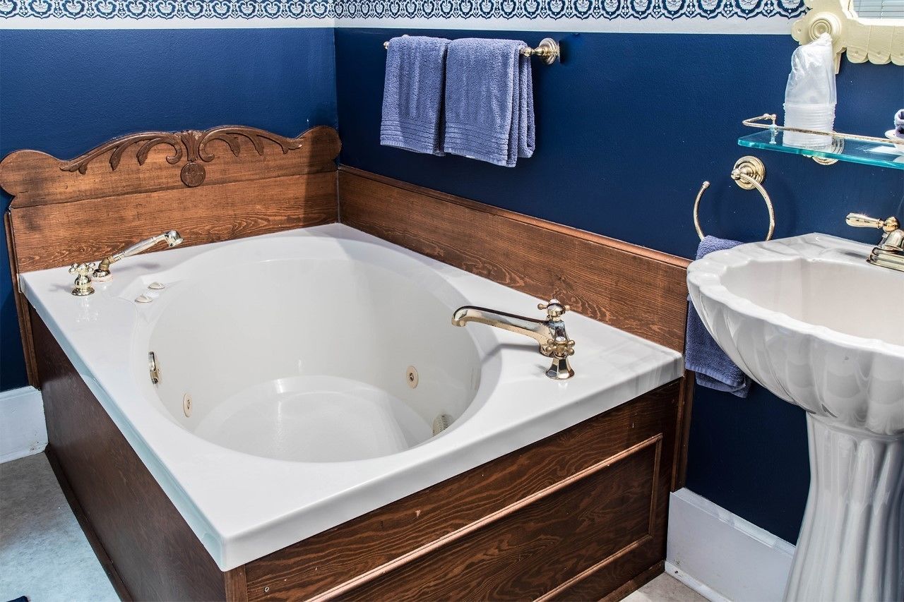 Un baño con cabecera de madera, una bañera blanca, un lavamanos blanco y una toalla azul en un perchero.