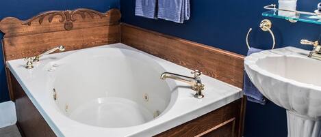 Un baño con cabecera de madera, una bañera blanca, un lavamanos blanco y una toalla azul en un perchero.