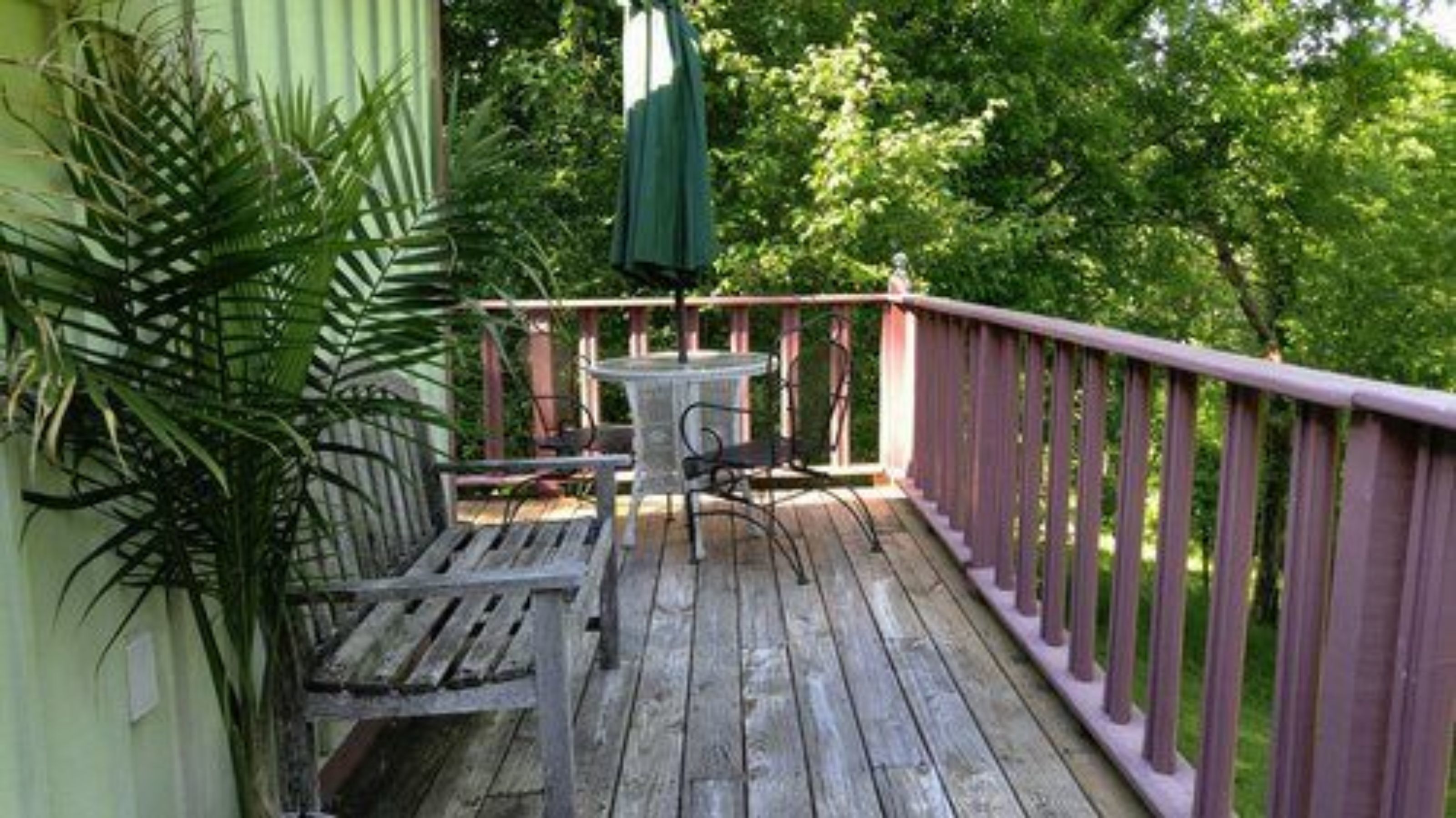 A wooden deck with a table and chairs, surrounded by a pink railing, and a green umbrella.