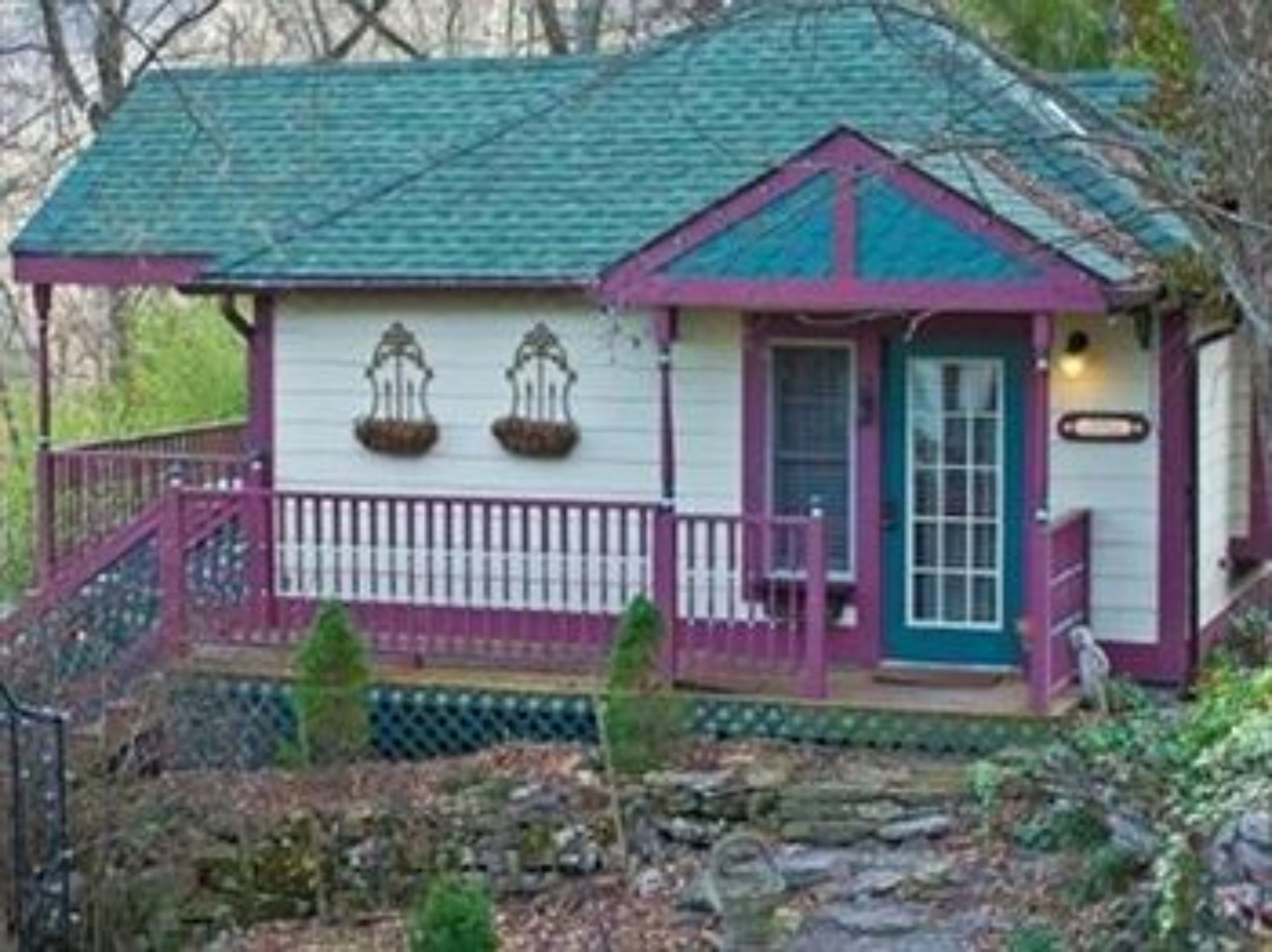 A small, single-story house with a green roof and a purple front porch.