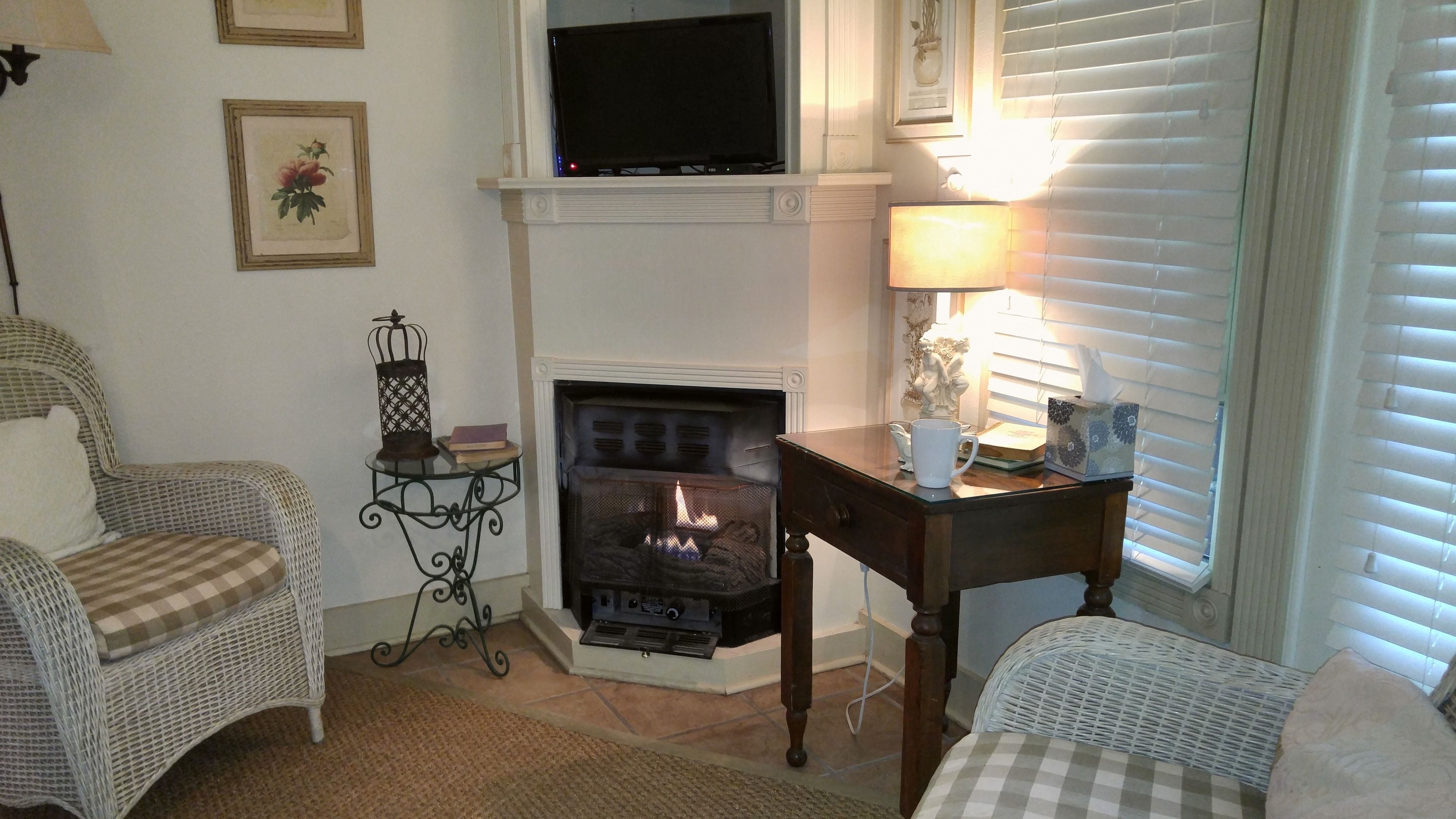 Una sala de estar acogedora con chimenea, sillones de mimbre, un televisor y una mesa con lámpara.
