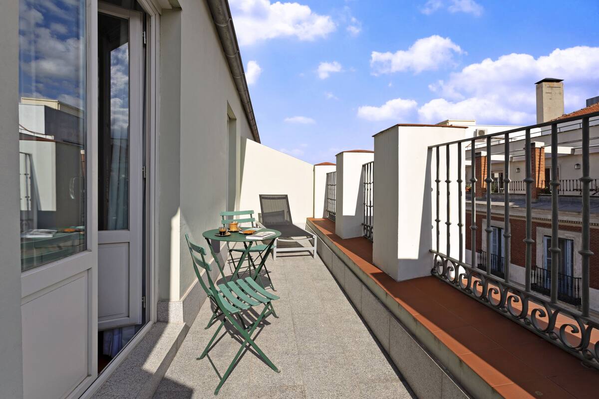 A balcony with a table and chairs, a glass door, and a view of neighboring buildings.