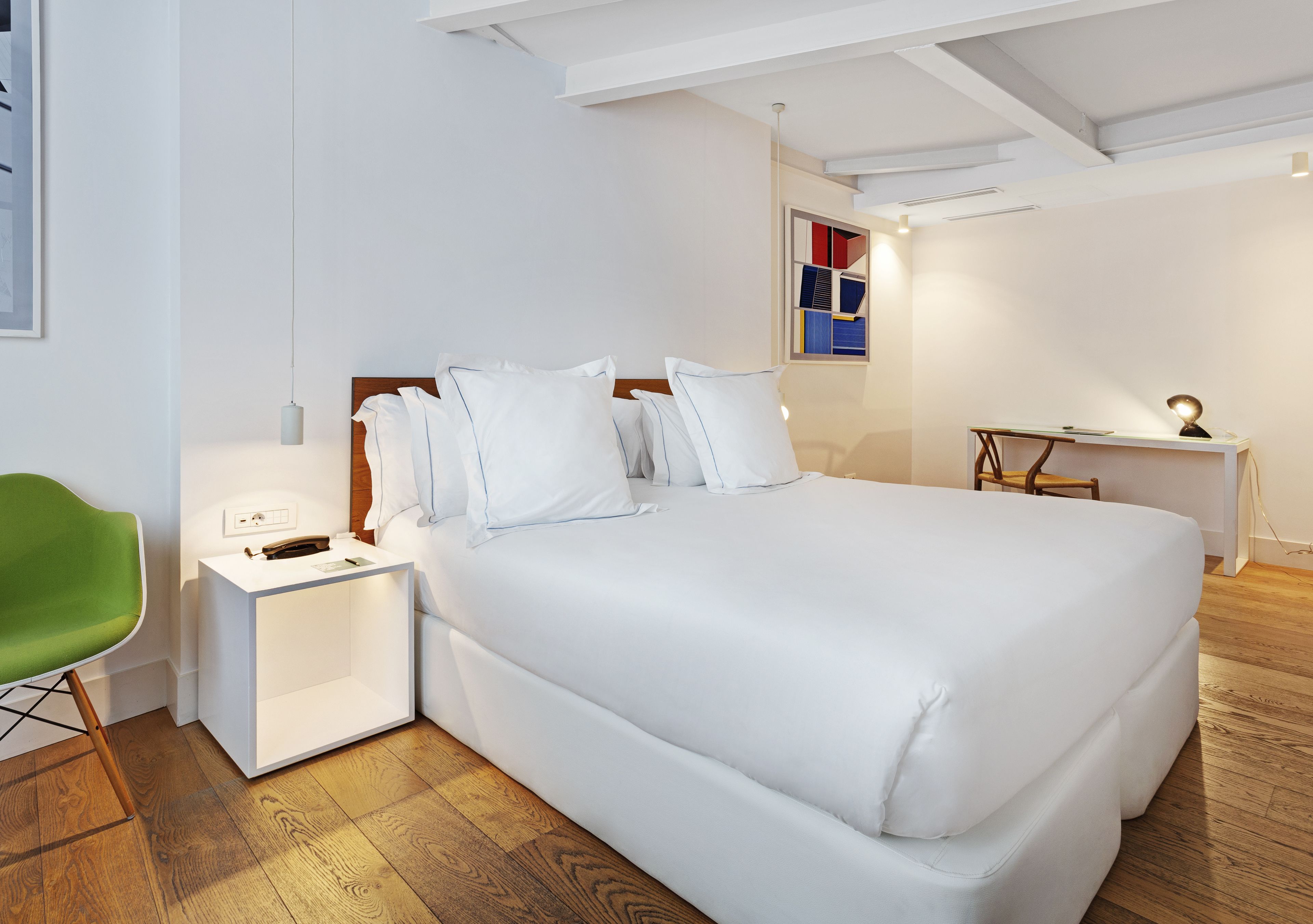 Une chambre bien rangée, avec un grand lit, des tables de chevet, un bureau et un fauteuil vert.