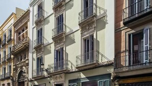A row of historic buildings with balconies, a shop on the ground floor, and a cobblestone street. - One Shot Prado (Madrid)