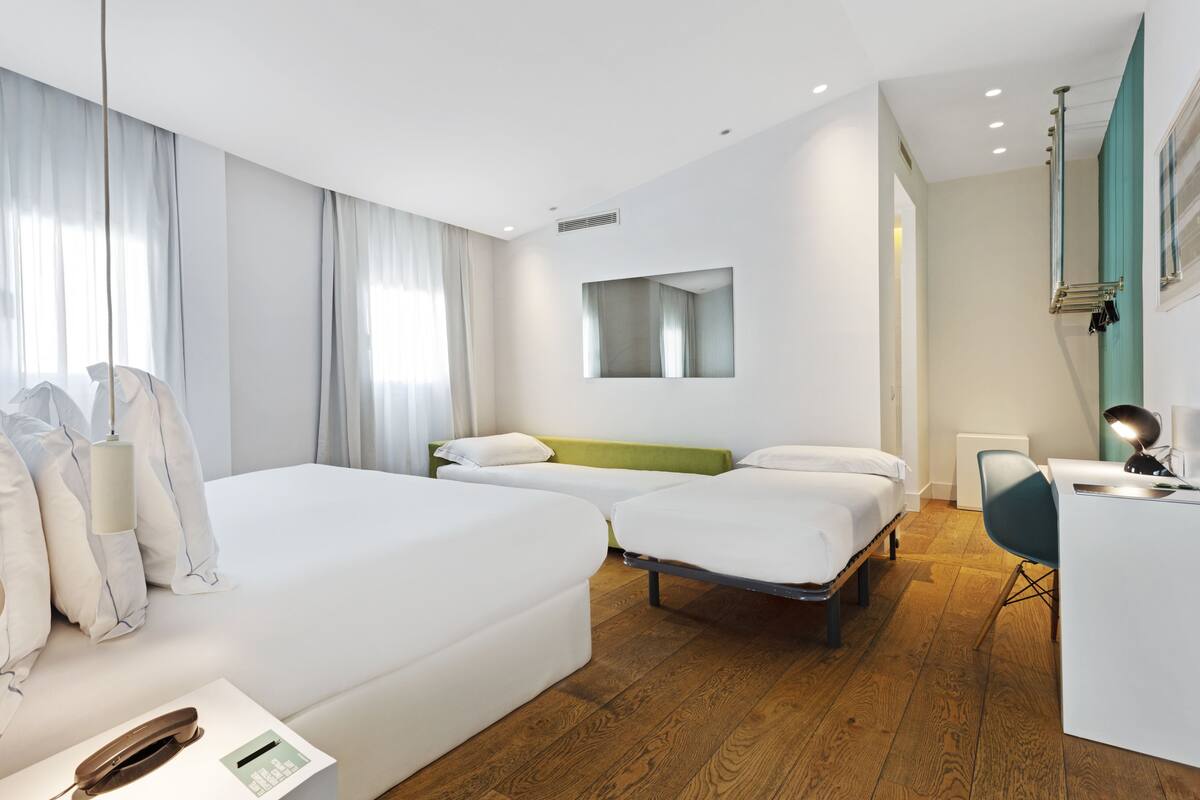 A modern hotel room with two single beds, a desk with a chair, and a large mirror on the wall.