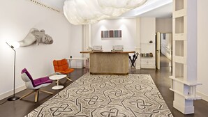 A modern interior with a reception desk, seating area, and a patterned rug. - One Shot Prado (Madrid)