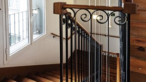 A wooden staircase with a wrought iron railing, a large arched window, and a wooden ceiling. - One Shot Prado (Madrid)