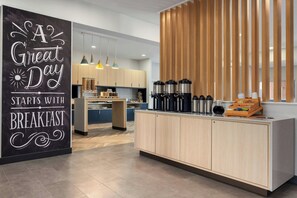 A modern kitchen with a breakfast bar, wooden cabinets, and a sign that reads 'A Great Day Starts with Breakfast.' - TownePlace Suites by Marriott Minot (Minot)