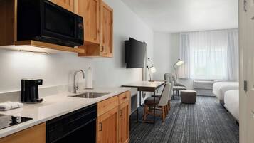 Een compacte hotelkamer met kitchenette, flatscreen televisie, bureau met stoel, bed en raam met gordijnen.
