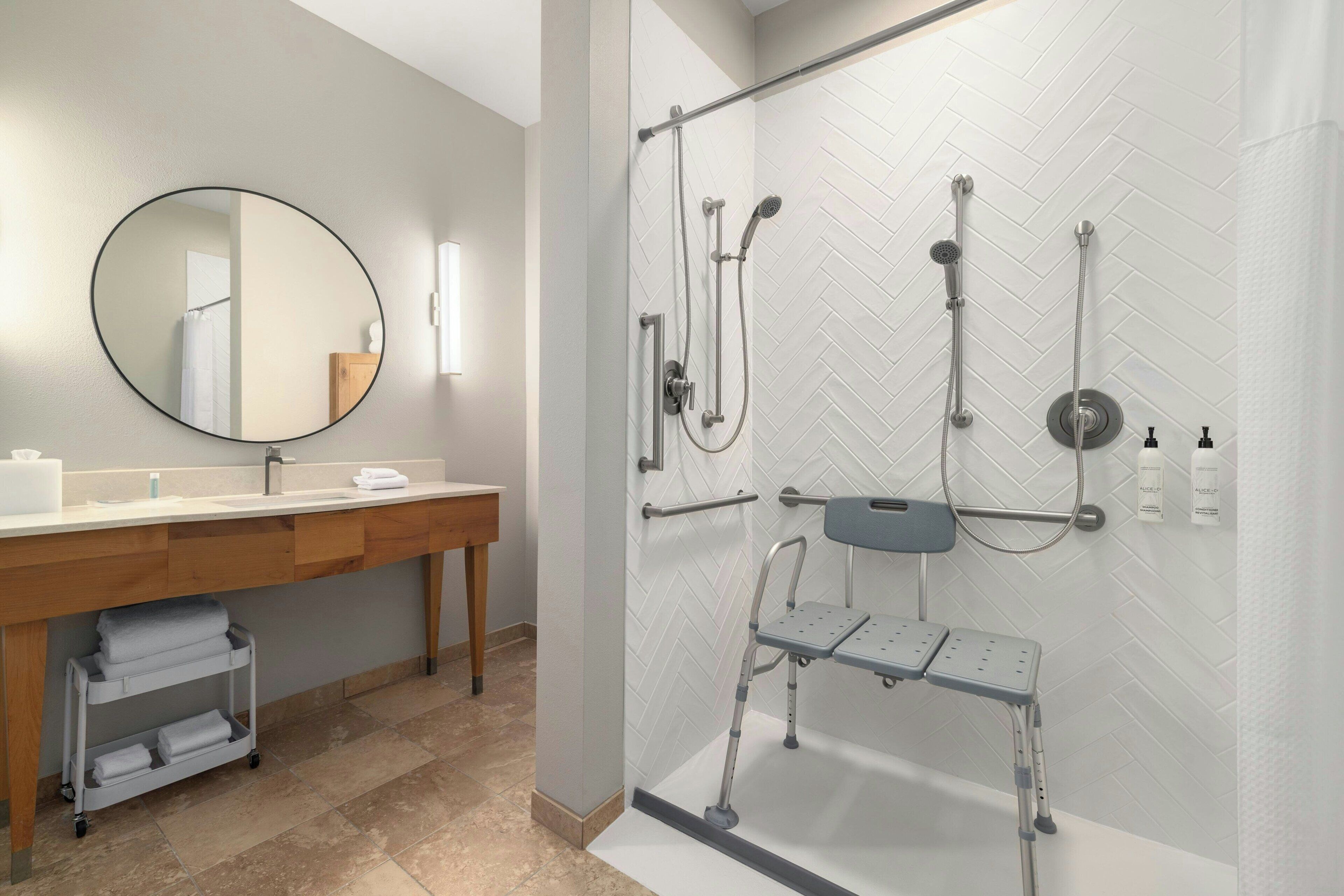 A modern bathroom with a shower, a sink, a mirror, and a bench.