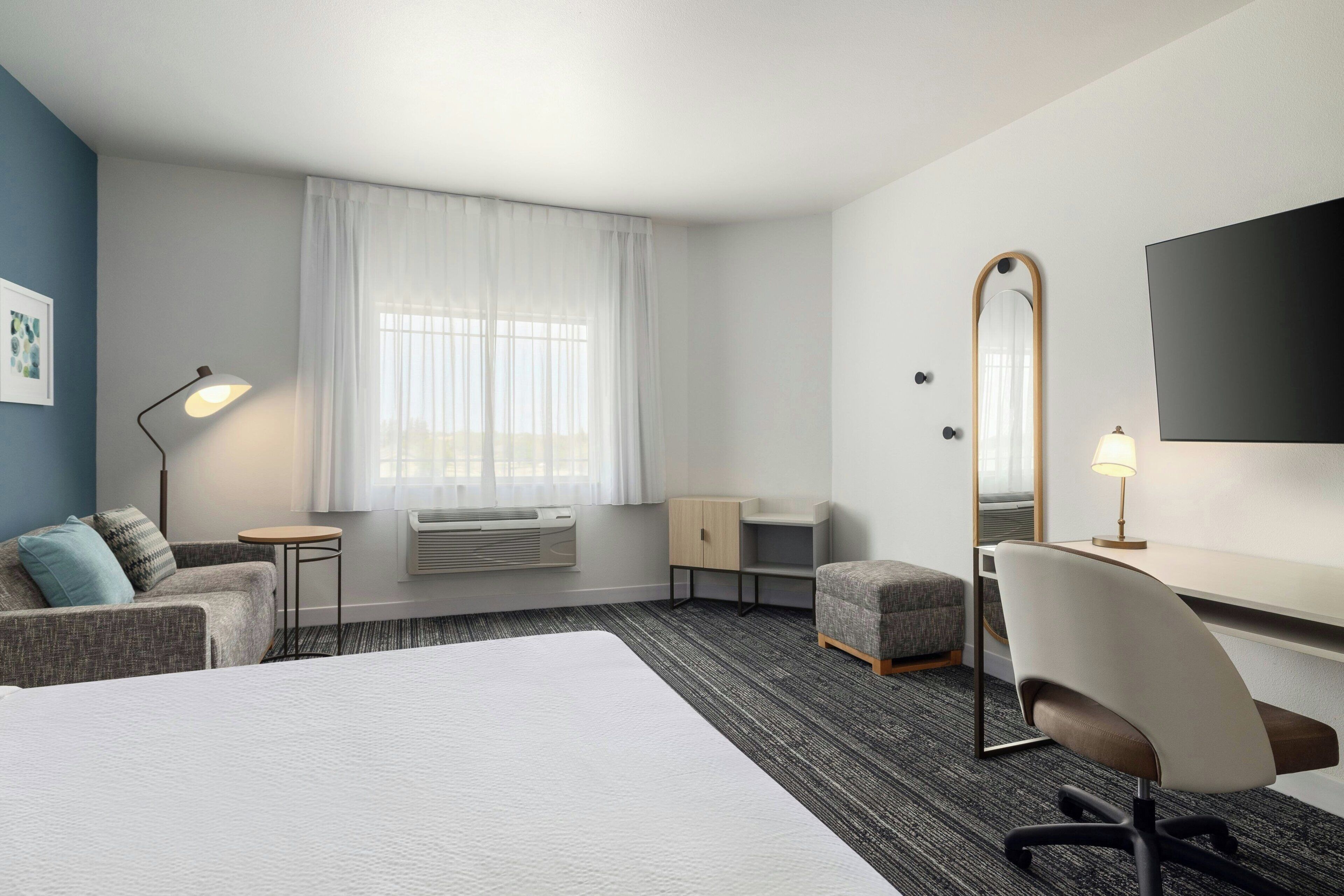 A hotel room with a bed, a desk, a chair, a television, and a window with curtains.