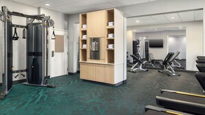 Un gimnasio con equipo de ejercicio, un armario de madera con toallas y un televisor.
