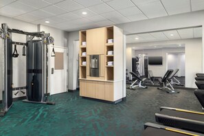 Un gimnasio con equipo de ejercicio, un armario de madera con toallas y un televisor.