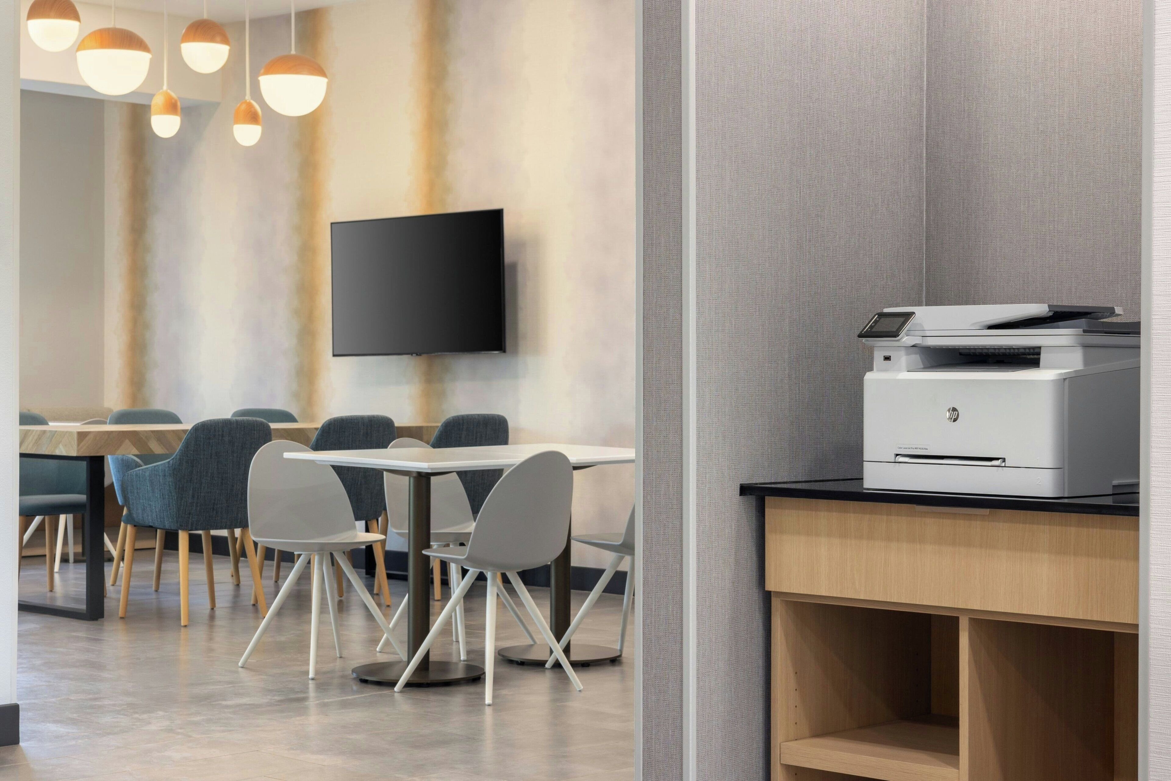 Un espace de bureau moderne doté d’un téléviseur à écran plat fixé au mur, d’une imprimante posée sur un bureau et d’une table de conférence avec des chaises.