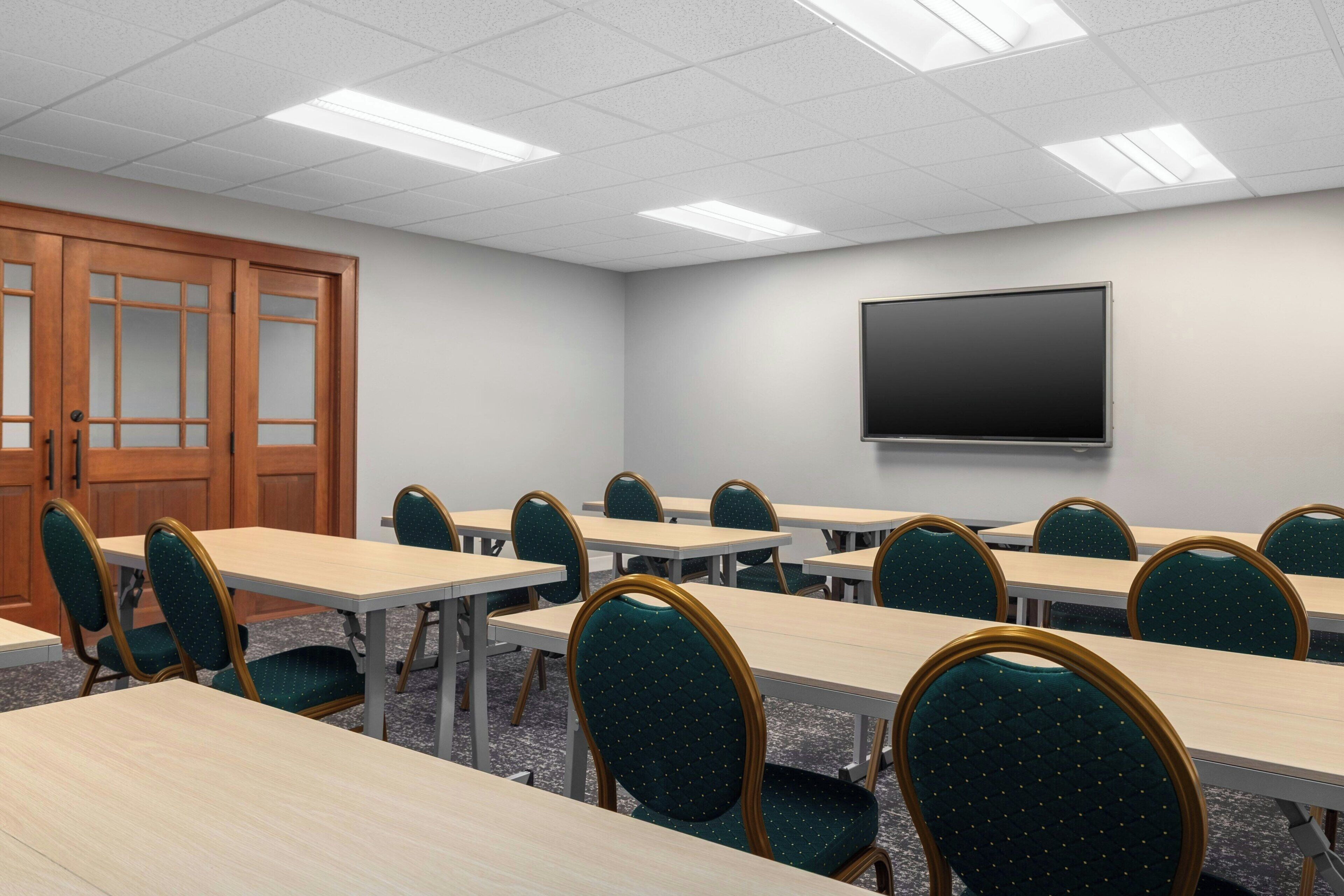 Un salón de conferencias con mesas y sillas, una puerta y una pantalla grande en la pared.