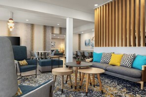 Un espacio lounge moderno con asientos, mesas y una pared decorativa.