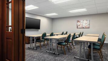 A conference room with tables, chairs, a projector screen, and a painting on the wall.
