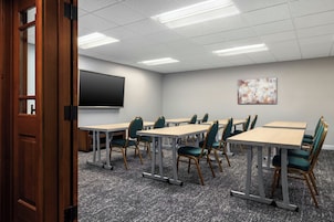 A conference room with tables, chairs, a projector screen, and a painting on the wall.