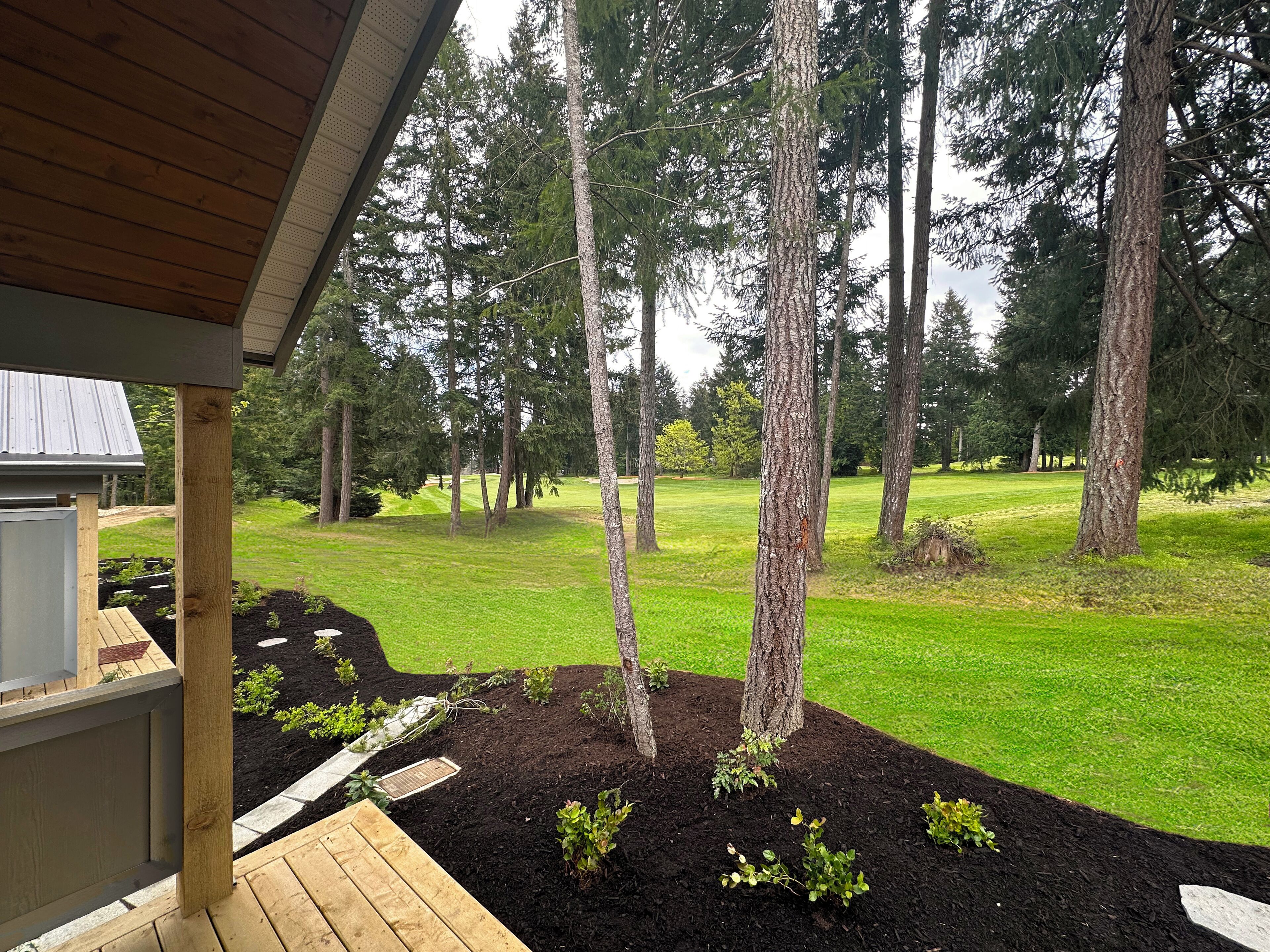 Vue d’un espace paysager agrémenté d’une terrasse en bois, d’une pelouse et de grands arbres.