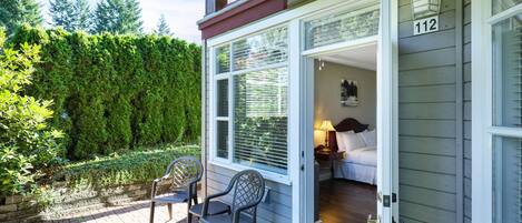 Une maison portant le numéro 112, une terrasse en bois avec deux chaises, et un jardin agrémenté d’une haie.