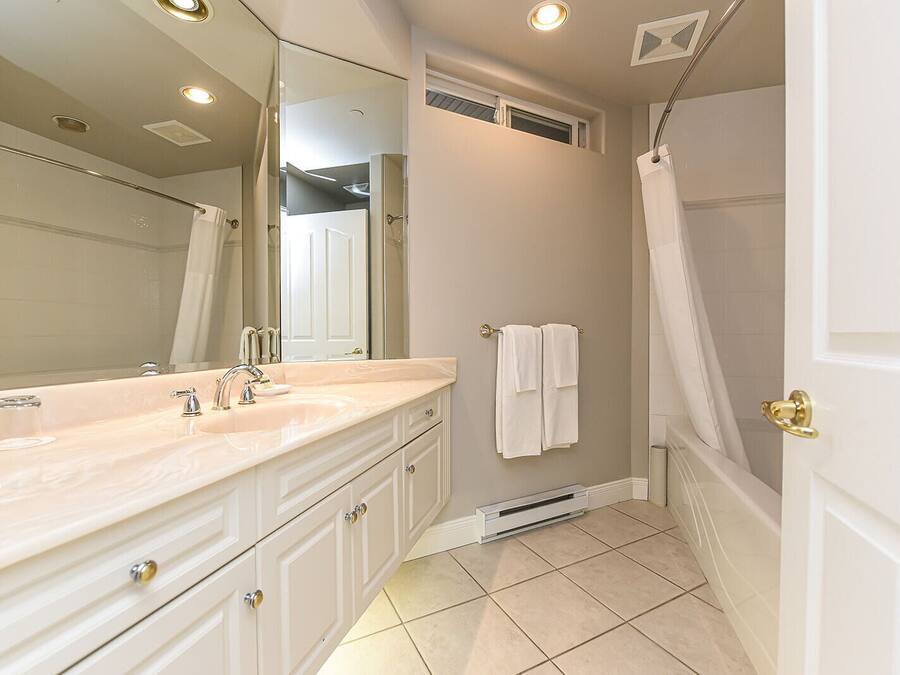 A bathroom with a large mirror, two sinks, a shower, and a door with a towel hanging on it.