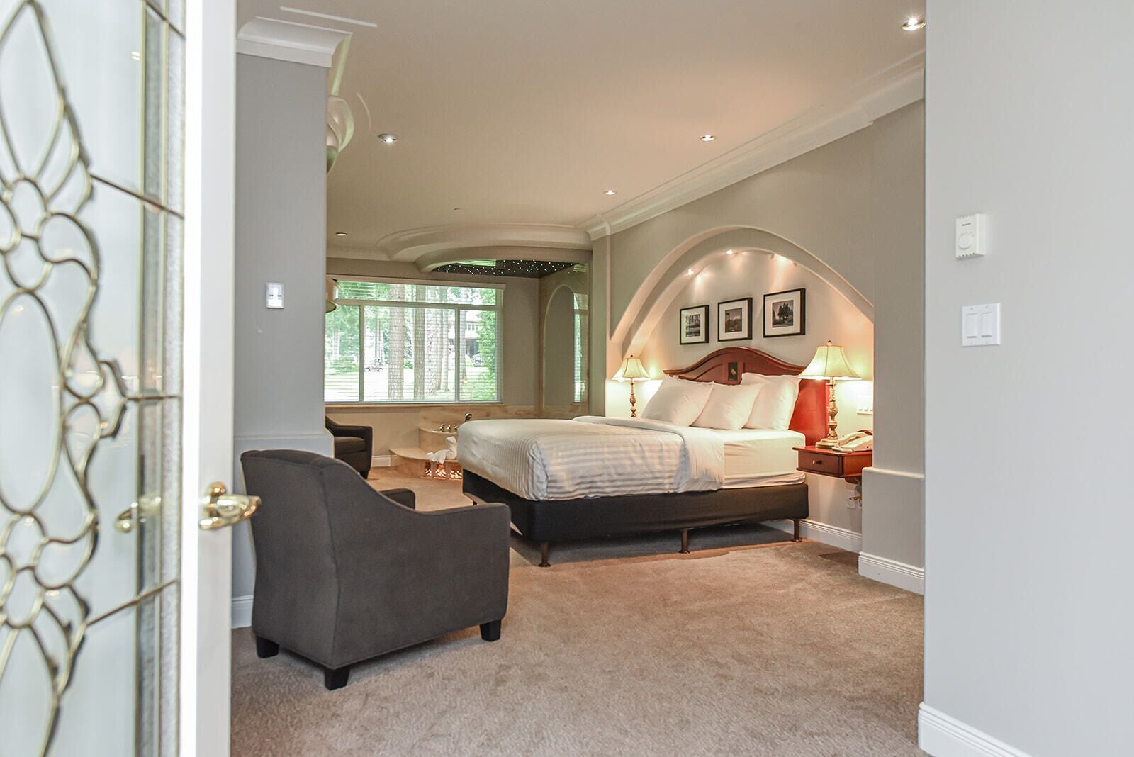 A bedroom with a bed, bedside tables, a chair, and a window with a view of trees.