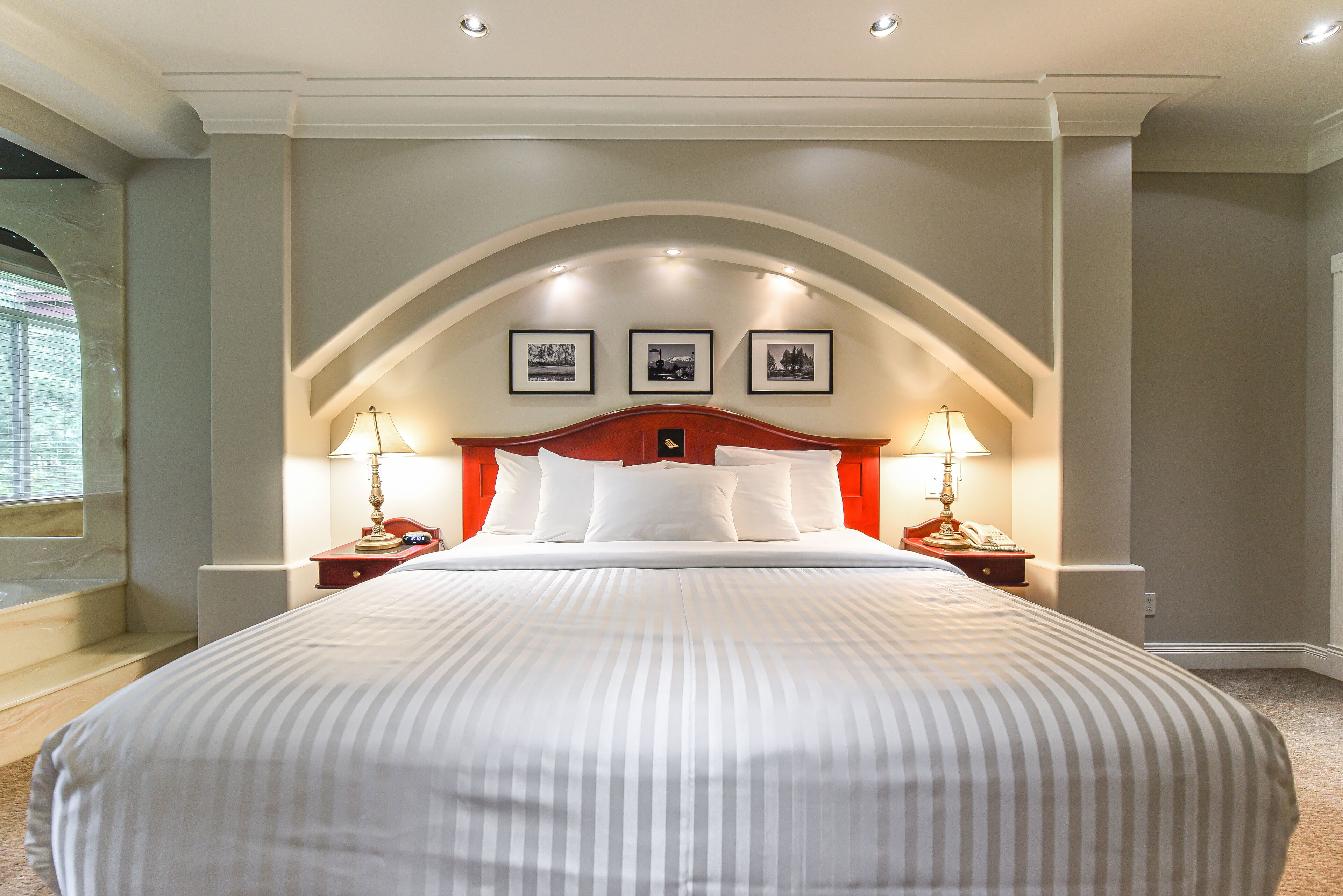A hotel room with a large bed, two bedside tables with lamps, a red headboard, and three framed pictures on the wall.