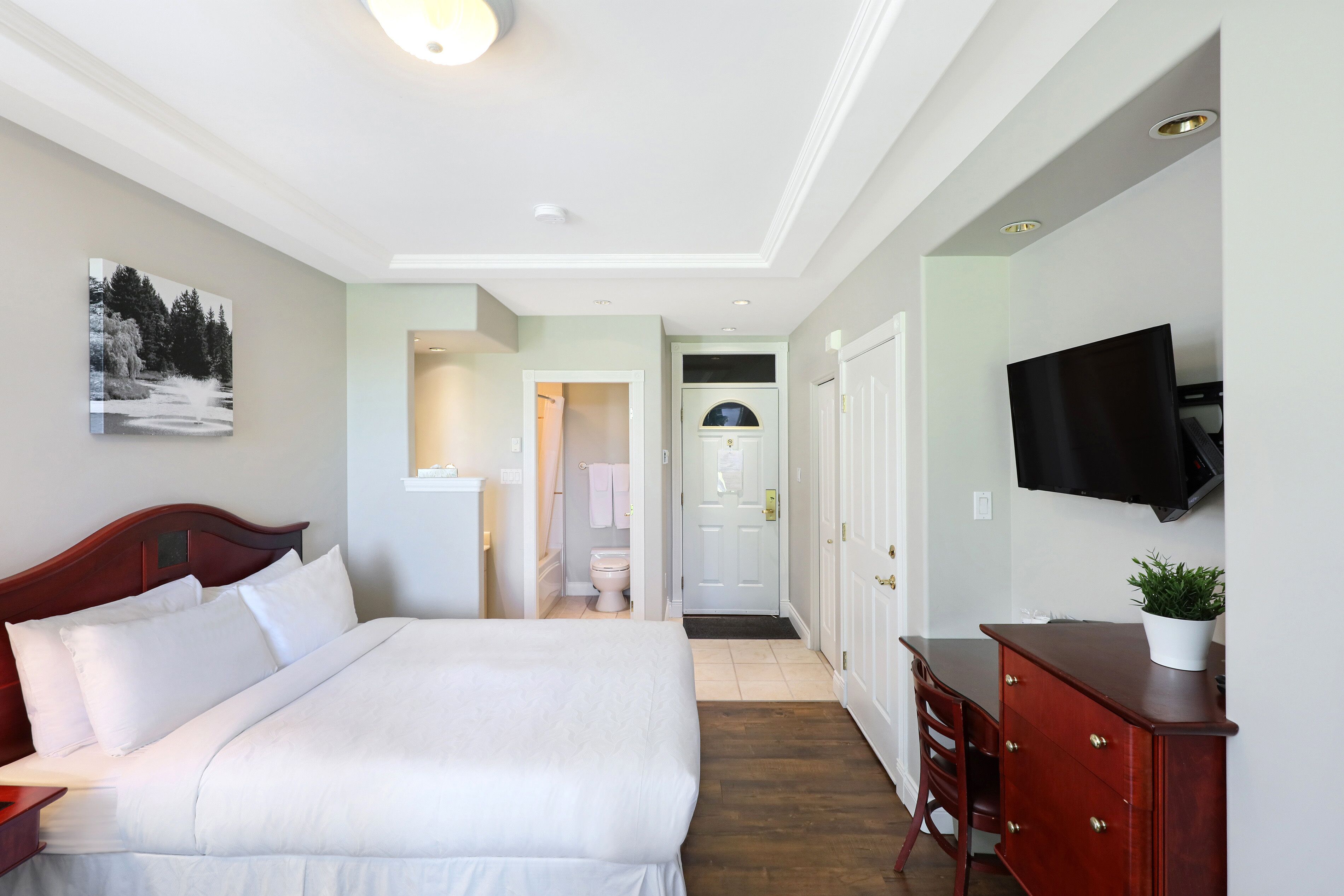 Habitación de hotel con una cama grande, un aparador de madera, un televisor montado en la pared y una puerta que da a un baño.