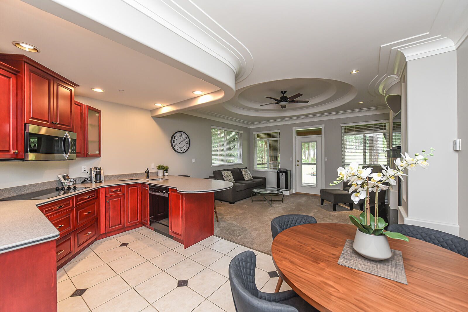 A modern kitchen with red cabinets, a microwave, and a dining area with a wooden table and chairs.