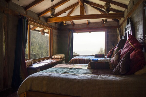 Un dormitorio rústico con vigas de madera, dos camas, un ventanal y vistas al exterior.