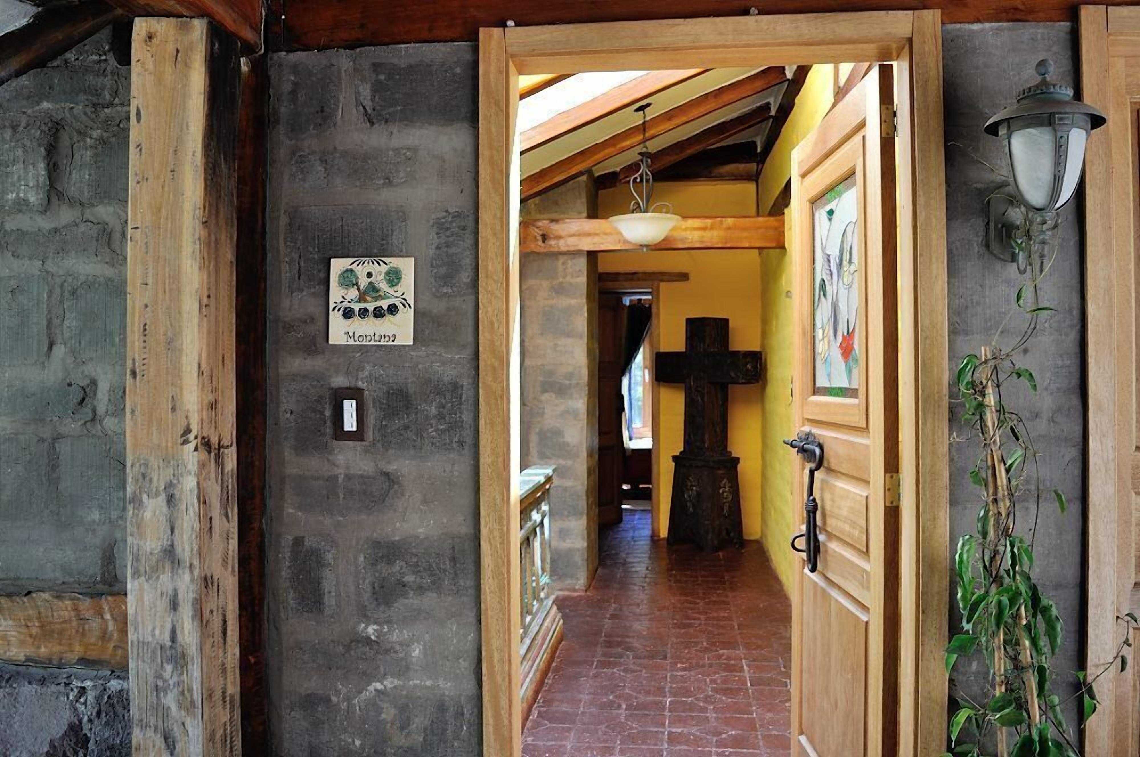 Un couloir avec une porte en bois, un mur en pierre, un luminaire suspendu et une croix sur le mur.
