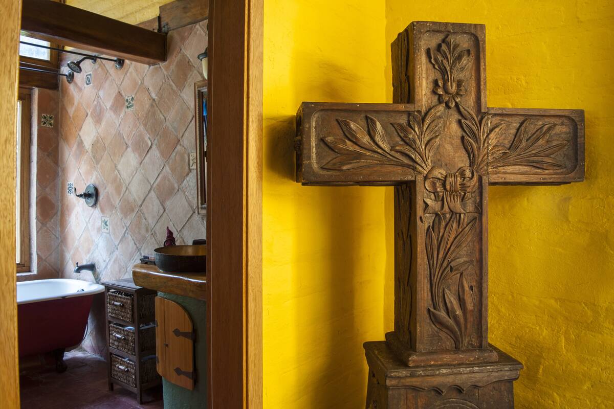 A bathroom with a red bathtub, a wooden cross, and a yellow wall.