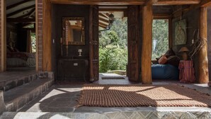 Un interior rústico de madera con piso de piedra, un espejo, un farol y vistas al exterior con vegetación.