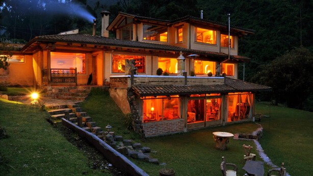 Una casa de dos pisos con un patio, mobiliario exterior e interior bien iluminado.