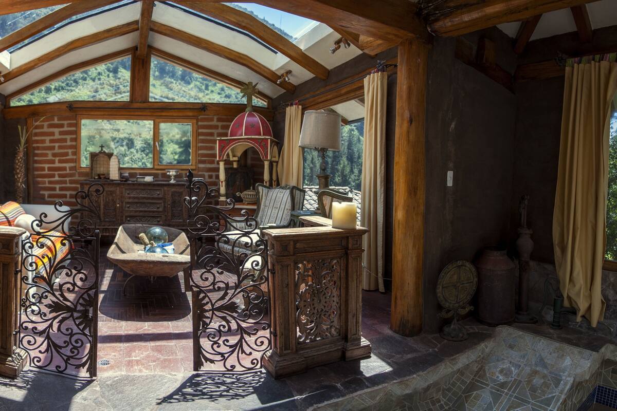 A rustic interior with a stone fireplace, wooden beams, and a view of the forest.