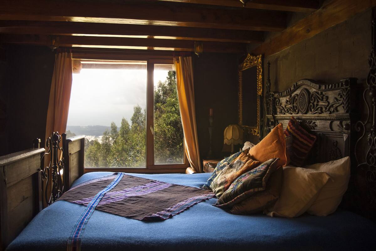 A bed with a view of trees through a window, a wooden headboard, and a patterned bedspread.