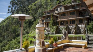 Un edificio de piedra con tejado de tejas rojizas, rodeado de abundante vegetación y una escalera de piedra que conduce a él.