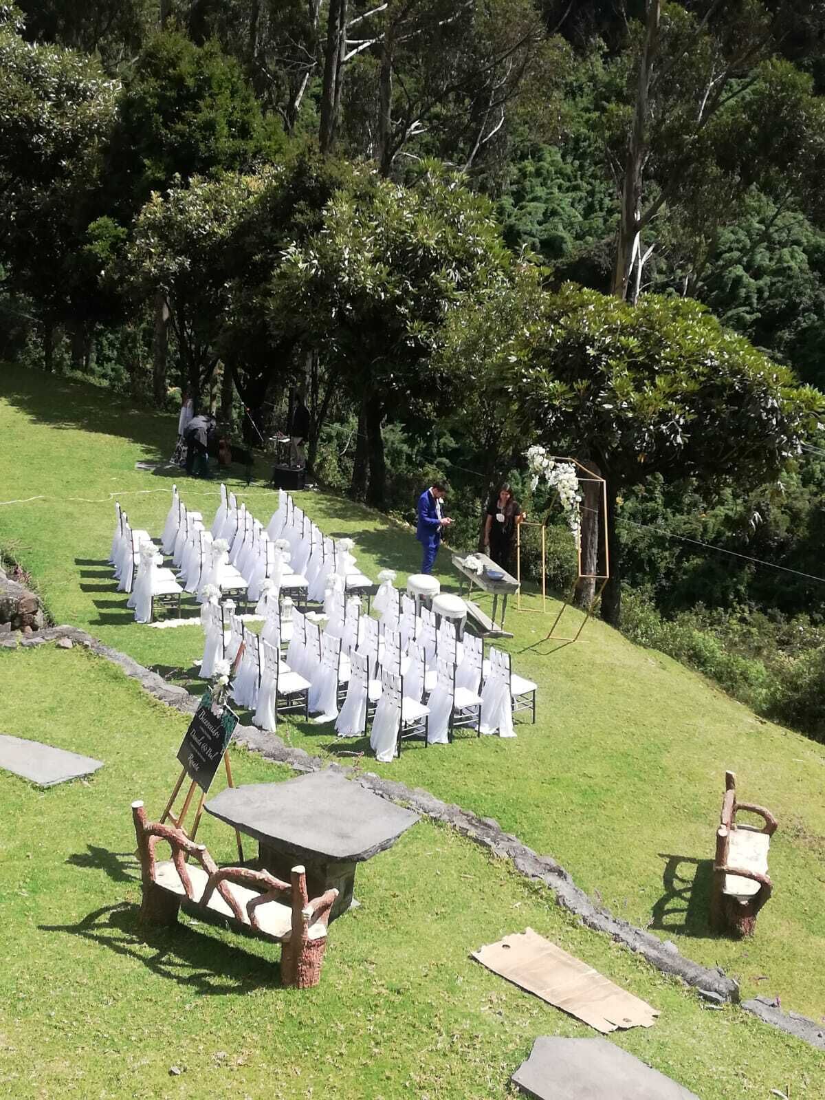 An outdoor event setup with white chairs arranged in rows, a wooden table, and a signboard.