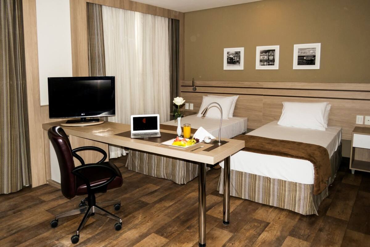 A hotel room with a bed, a desk with a laptop, a TV, and a chair.