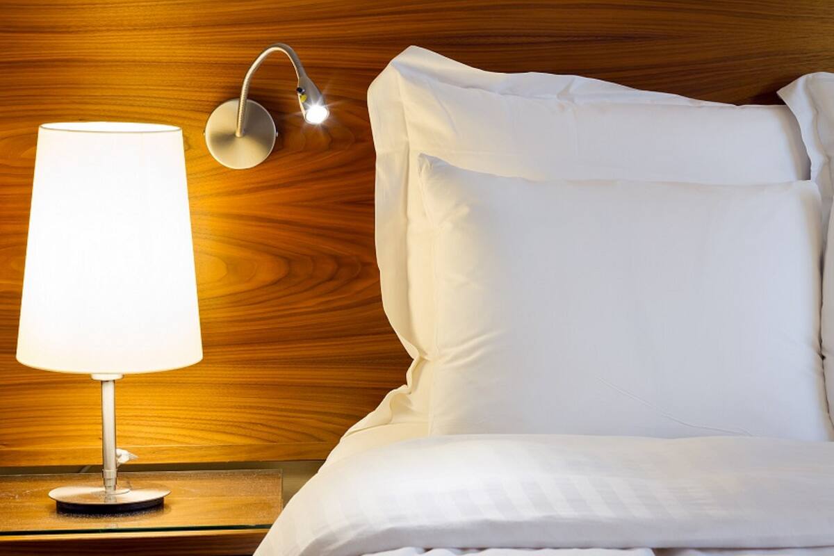 A neatly made bed with white linens, a bedside lamp, and a wall-mounted light fixture.