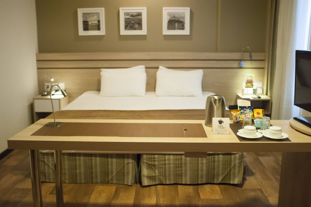 A hotel room with a bed, bedside table, lamp, and a small table with cups and a teapot.
