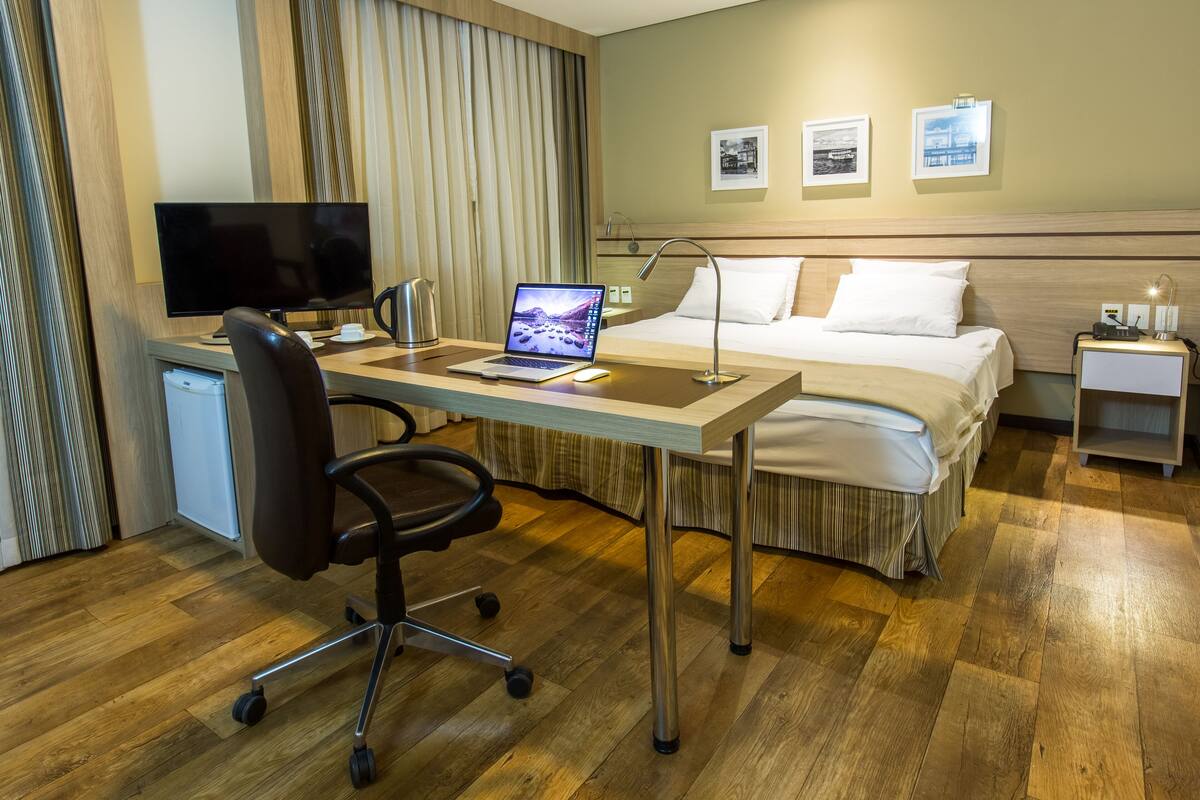 A hotel room with a bed, desk, chair, and a television.