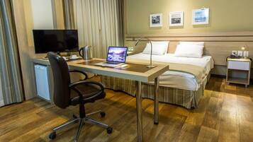 Quarto de hotel com cama, escrivaninha, cadeira e televisão.