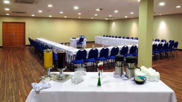 A conference room with rows of blue chairs, white tables, and a wooden floor.