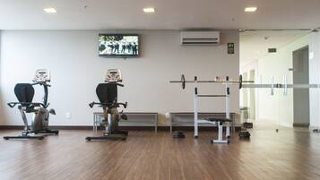 Ein Fitnessraum mit Trainingsgeräten, einem Fernseher an der Wand und einer Sitzbank.