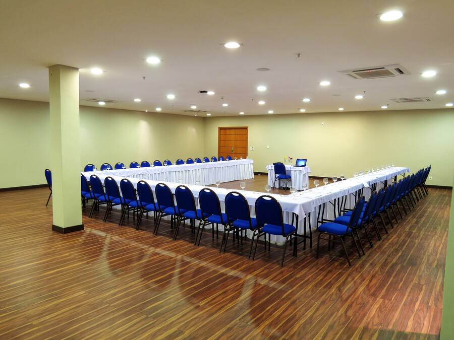 A conference room with long tables and blue chairs, equipped with ceiling lights and an air conditioning unit.